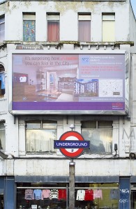 "It's surprising how at home you can feel in the city", reads this billboard placed in a visibly run-down area of  London, above the iconic sign of a tube station (Aldgate East in Whitechapel High Street), at the boundary with the City. The ad was commissioned by Berkeley Homes and displayed by Primesight. A clothing store is visible at the ground floor of the building. Overall, the image focuses on the contrast between the rich shown in the billboard and the poor shown by real London.