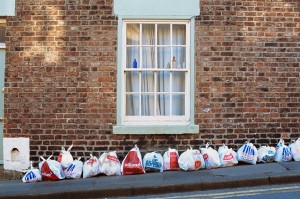 Durham, England - May 2, 2012: Most British supermarket chains (Pooundland, Tesco, Iceland, Wilkinson) are portrayed by these shopping bags used to wrap garbage and left out on the street (Allergate) for collection. A small collection of glass bottles is displayed at the window.